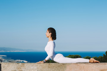 Fototapeta na wymiar Side view shot young woman with perfect strong body practicing yoga on a sunny day with amazing sea view on background, woman seeking enlightenment through meditation, stretching exercise yoga pose