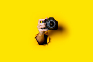 Man's hand holding a camera on a bright yellow background. - obrazy, fototapety, plakaty