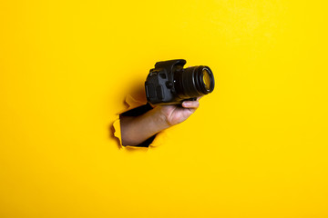 Man's hand holding a camera on a bright yellow background.
