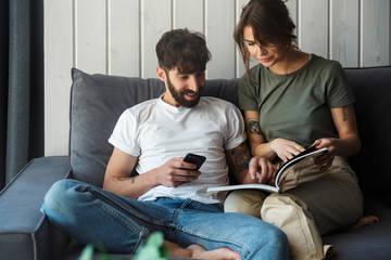 Lovely young couple relaxing on a couch at home, reading magazine