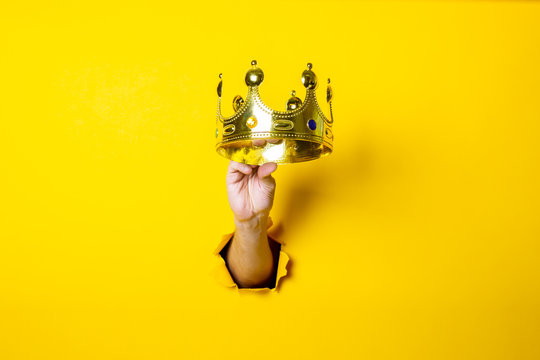 Female hand holds a gold crown on a bright yellow background.