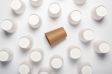 Many white and one brown paper cups on a light background. Top view, flat lay.