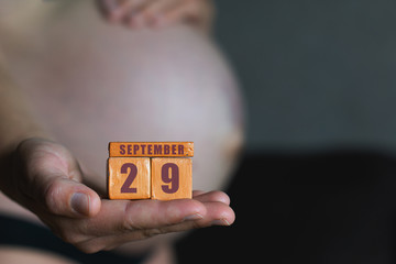 september 29th. Day 29 of month,planned date of birth. Month and day placed on wood calendar in pregnant womans hand. autumn month, day of the year concept