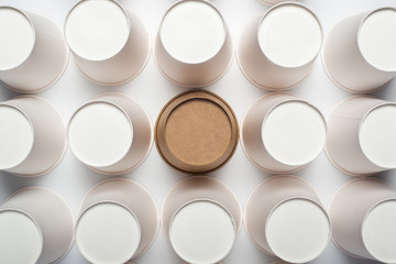 Many white and one brown paper cups, flipped upside down on a light backgroundon a light background. Top view, flat lay.