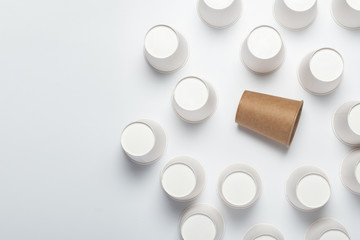 Many white and one brown paper cups, flipped upside down on a light background. Top view, flat lay.