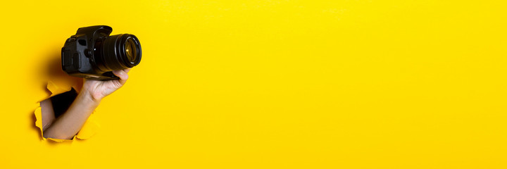 Female hand holding a camera on a bright yellow background. Banner.