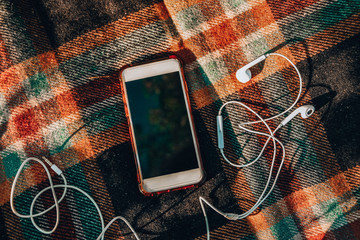 Smartphone with headphones on the cozy sweaters. Top view. Autumn flatlay. Outdoor listening...