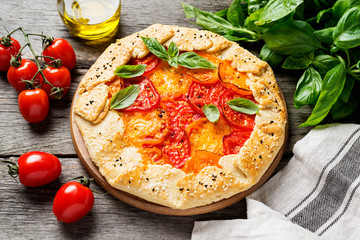 Delicious homemade rustic open pie (galette) with colorful tomatoes and basil leaves .