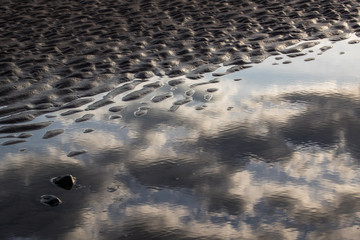 abstract clouds reflected in beach pond water during sunrise