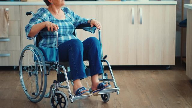Sad handicapped elderly woman in wheelchair sitting alone in kitchen. Senior pensioner after injury and rehab, paralysis and disability for depressed invalid full of sorrow, worry and sad face