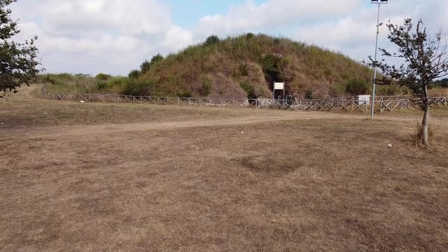 Ancient tomb, tumulus. Archeological and necropolis catacombs site. Etruscan archeological site. Aerial view of single tomb, moving forward to the tomb. Cerveteri, Italy