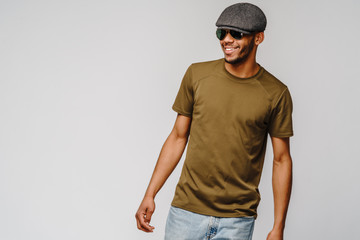 african-american young man in green t-shirt wearing sunglasses and cap over light grey background with copy space