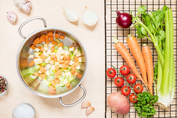 Top view of a saucepan and a variety of fresh raw vegetable ingredients for making vegetable soup.