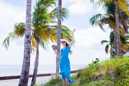 Happy woman holding the coconut next to the palms on the island