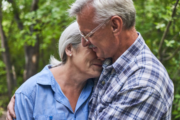 Close-up portrait of elderly couple in love on romantic date in summer park smiling and hugging against the background of green trees