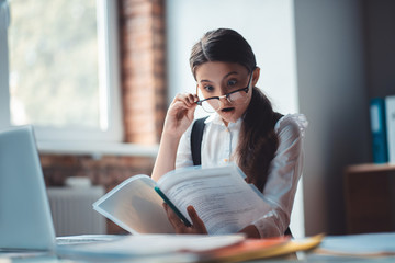 Brunette girl in eyeglasses reading a report and looking shocked