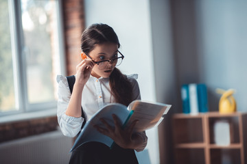 Brunette girl in eyeglasses reading a report and looking surprised