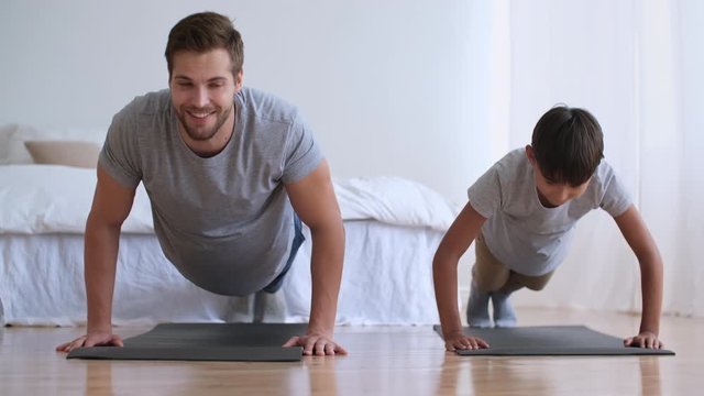 Family fitness at home, Father coach, Sports kid, Fun gymnastics. Dad and son are doing physical exercise pushing up from the floor at home