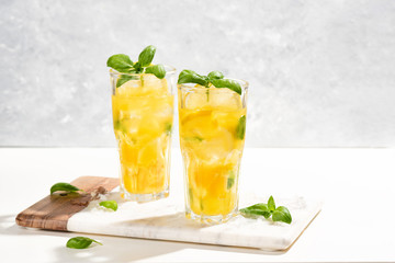 Citrus lemonade or mojito cocktail with lemon and orange and basil. Cold beverage or drink with ice on marble cutting board