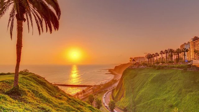 Aerial sunset view of Lima's Coastline in the neighborhood of Miraflores timelapse with orange light, Lima, Peru. Road with traffic and beach with ocean. Palm near Love park