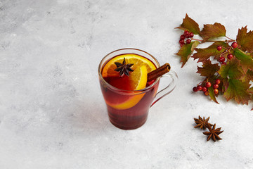 Hot red autumn mulled wine in mug with spices and orange on grey background.