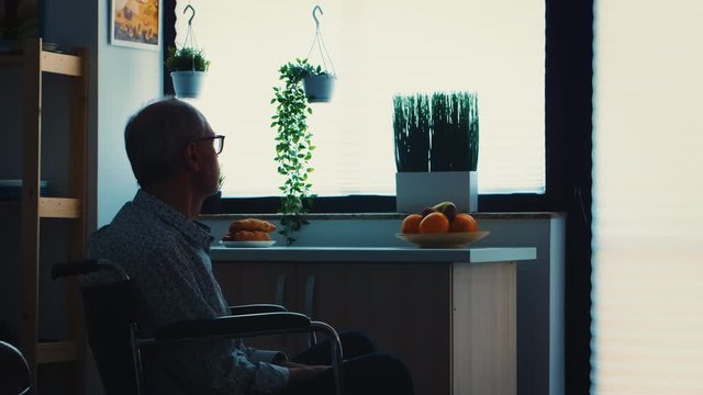 Lonely handicapped pensioner in wheelchair worrying about his life. Elderly handicapped pensioner after injury and rehab, paralysis and disability for depressed invalid full of sorrow, worry and sad
