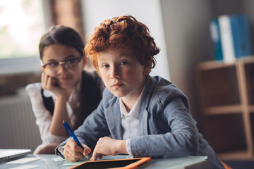 Red-haired boy studying with his friend and looking thoughtful