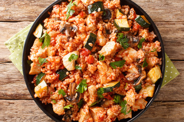 Fried rice with chicken, zucchini and mushrooms tomatoes close-up in a frying pan on the table. horizontal top view from above
