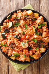 Mediterranean rice with chicken, zucchini and mushrooms in tomato sauce close-up in a frying pan on the table. Vertical top view from above