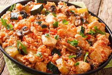 Fried rice with chicken, zucchini and mushrooms tomatoes close-up in a frying pan on the table....