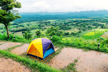 Camping tent that is set up at the highest point of a high mountain with a backdrop of sky and mountains.