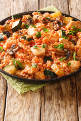 Spicy rice with chicken, zucchini and mushrooms in tomato sauce close-up in a frying pan on the table. vertical