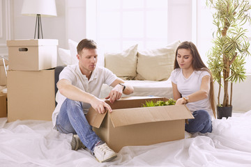 Portrait of happy couple looking at laptop computer together sitting in new house, surrounded with boxes