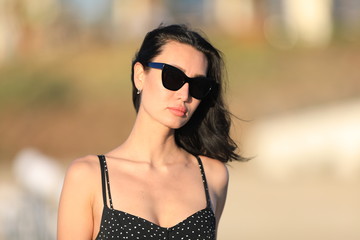 portrait of a beautiful brunette girl in sunglasses in a black dress in summer