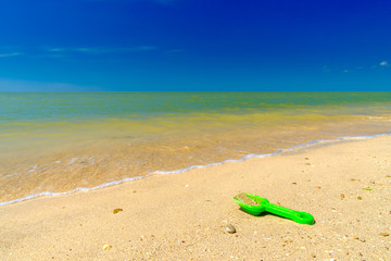 Green plastic baby scoop in the sand on the sea beach. The concept of a seaside vacation with children during vacation. Summer sunny day at the seaside resort. Blue sky and calm sea. Copy space. 