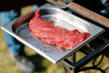 Concept of the correct cooking of meat. The chef prepares, fries a beef steak in the open air. Raw fresh steak served with pepper and salt.