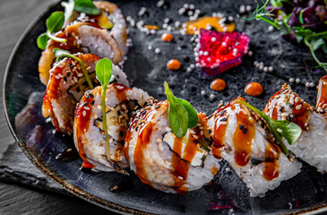 sushi roll with cream cheese, cucumber and eel in plate on black wooden table background