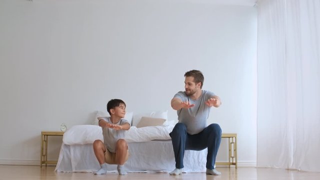 Family fitness at home, Father coach, Sports kid, Fun gymnastics. Sportive dad and son doing physical exercise squatting together while standing on the floor at home