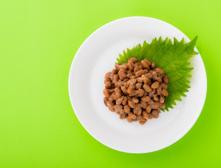 白いお皿の上に乗った納豆。緑の背景。