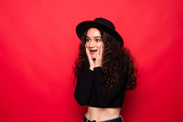 Portrait of happy screaming surprised young woman standing isolated over red background. Looking aside.