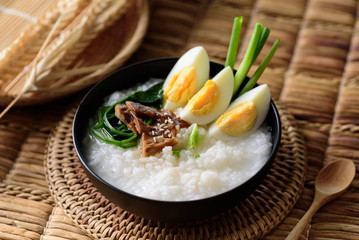 Asian food, Rice soup with boiled egg, grilled mushroom and spinach in a bowl on woven rattan sheet