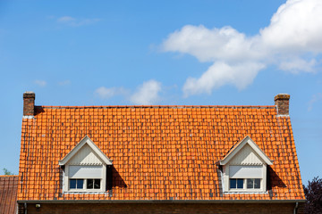 Symmetric red tiled roof with two dormers with rolling shutters and two chimneys in the Netherlands