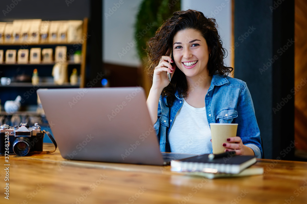 Wall mural portrait of smiling hipster girl looking into camera while having mobile conversation on mobile smar
