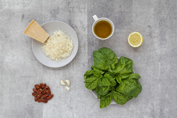 Flat lay of fresh ingredients to prepare pesto Basil Toscano, pecan nuts, parmesan cheese, olive oil, lemon juice and garlic. Gray plates and background table.