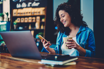 Cheerful skilled female freelancer dressed in casual clothes sending funny messages to friends...
