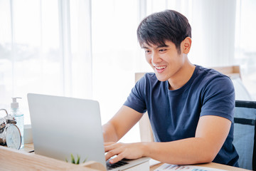 Happy Asian man using Laptop computer and checking good News, Trading, Watching Movie in the Bedroom. COPY SPACE. WORK FROM HOME Concept.