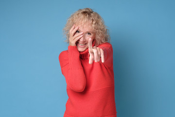 Senior caucasian woman pointing at you. Studio shot on blue wall.