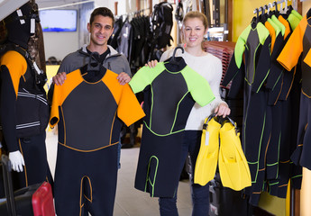 Sporty woman and man are satisfied of new costumes for diving and flippers in the store. © JackF