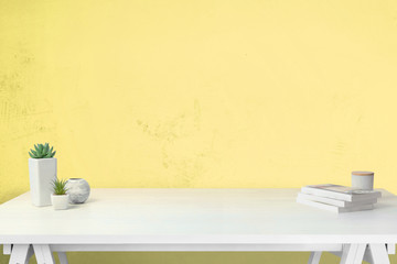 Work desk with free space for product promotion. Yellow wall in background. Books and plants on the table. Front view