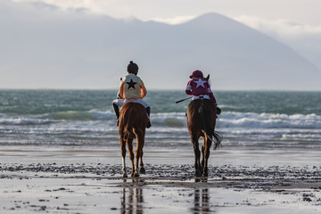 Two race horses and jockeys looking out at the ocean on the west coast of Ireland